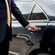 A professional driver in a suit opening the rear door of a luxury sedan